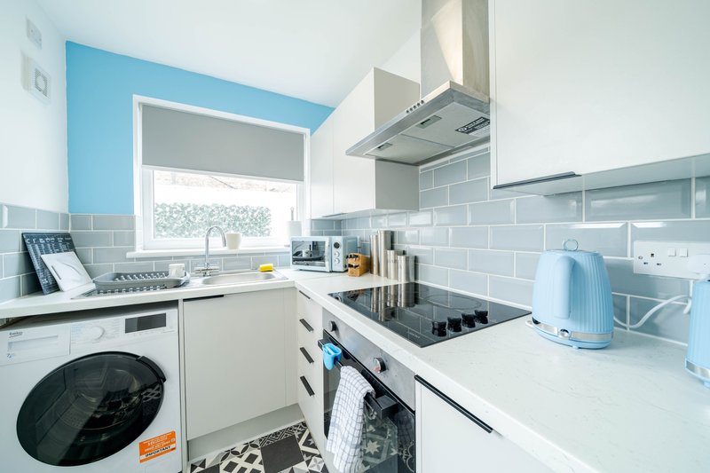 Modern kitchen with blue accent wall, white cabinetry, gas hob, and integrated appliances