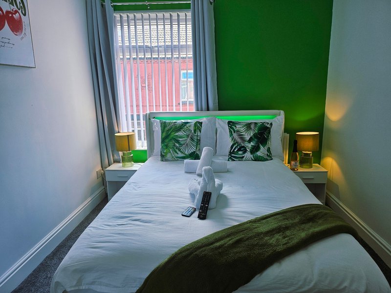 Modern bedroom with double bed, green accent wall, patterned cushions and bedside lamps