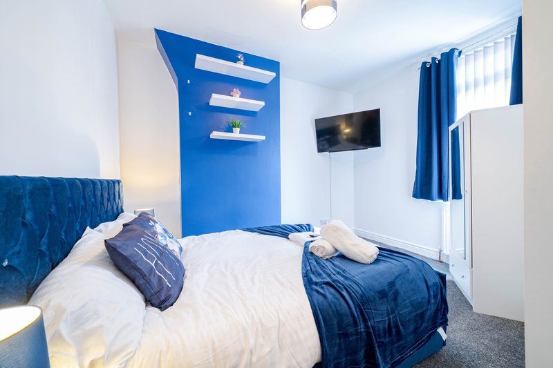 Modern bedroom with double bed, blue feature wall, shelving, and wall-mounted TV