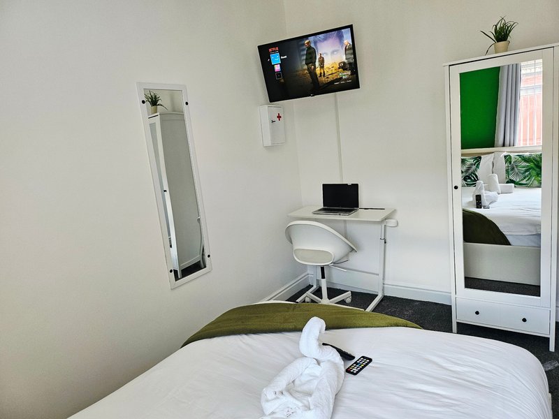 Bedroom with single bed, desk with laptop, wall-mounted TV and mirror
