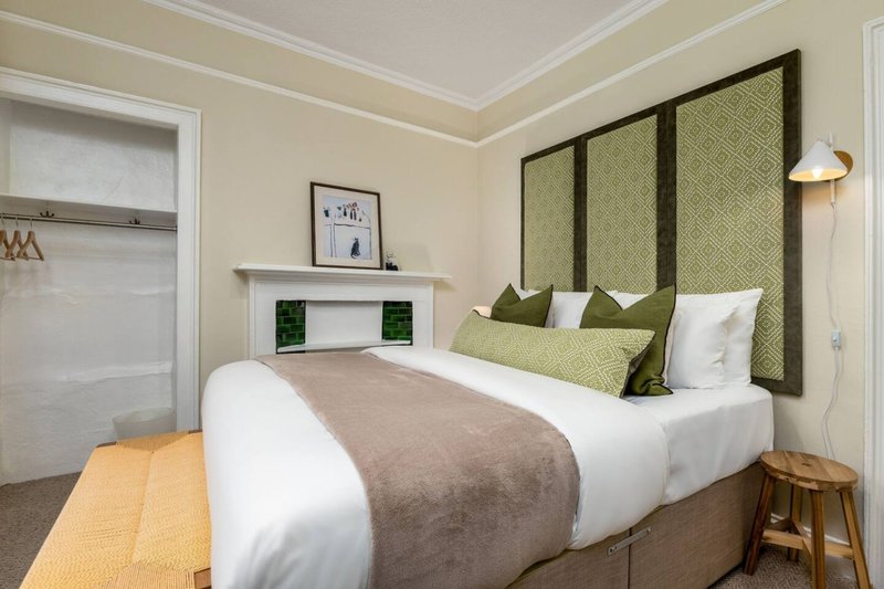 Modern bedroom with double bed, olive-green headboard, white bedding and wooden bedside table