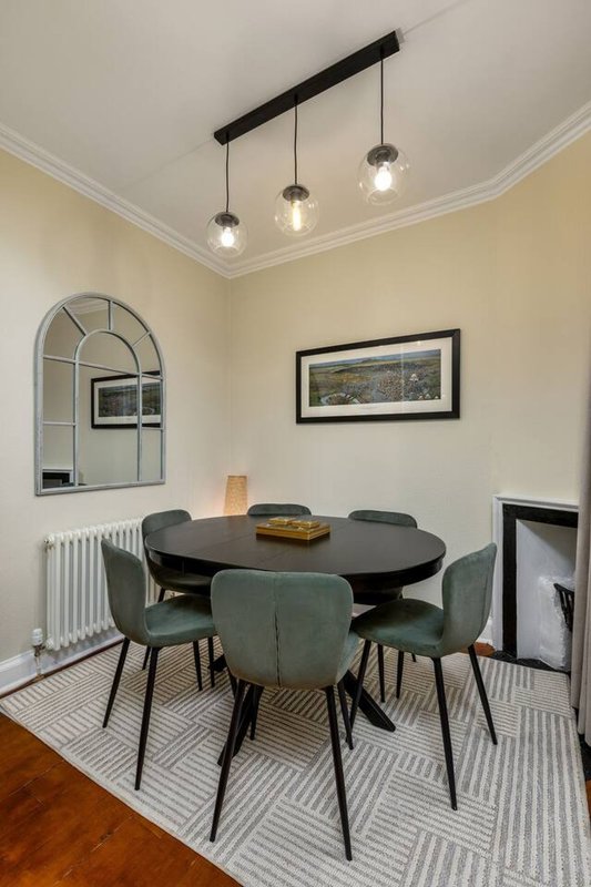 Dining room with round black table, four green chairs, pendant lights and arched mirror