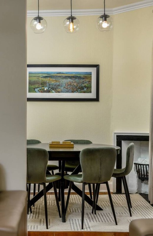 Modern dining room with round black table, green chairs, pendant lights and framed landscape artwork