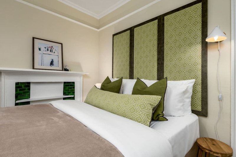 Modern bedroom with white bed, olive-green upholstered headboard, fireplace and floor lamp
