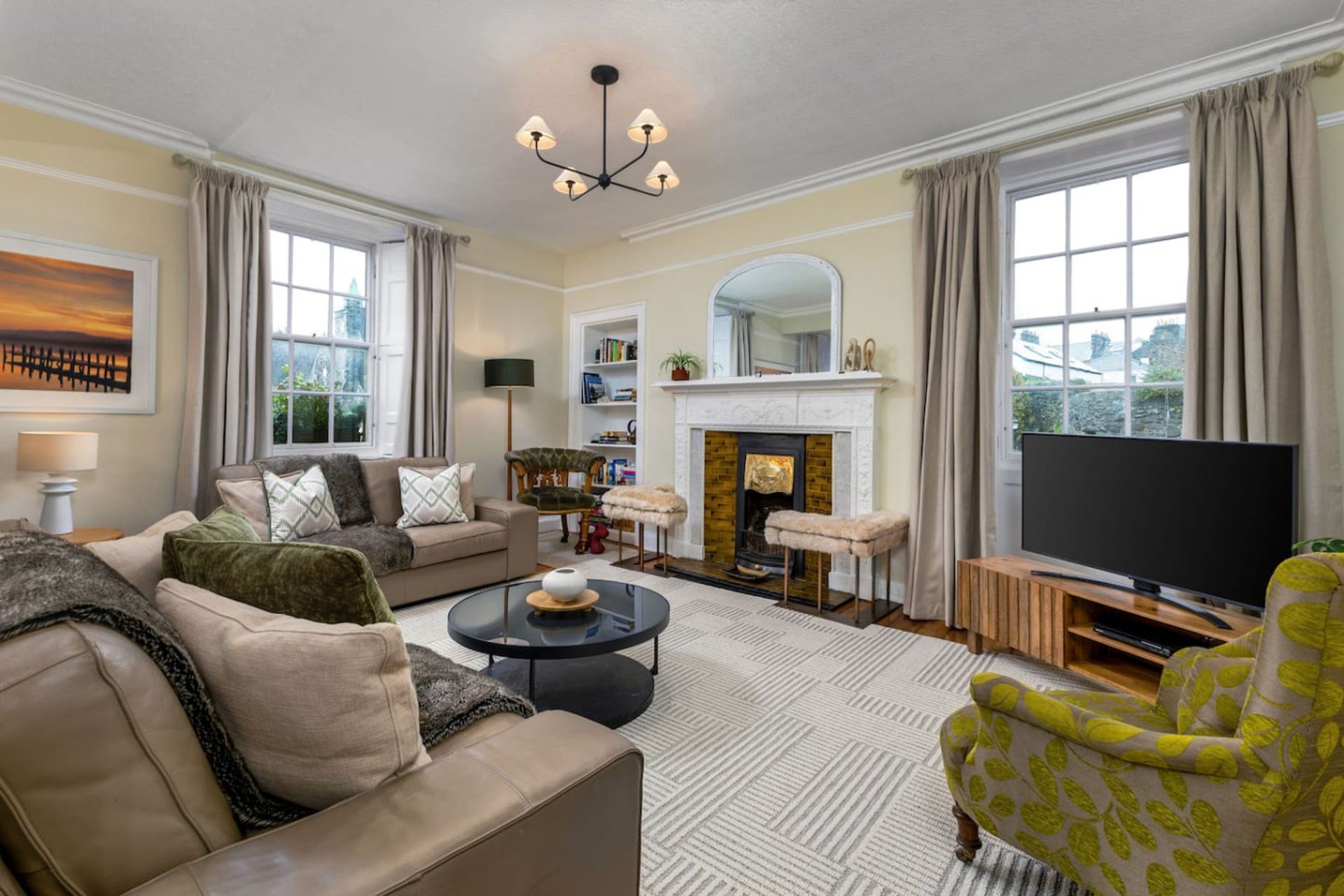 Spacious living room with fireplace, sofas, round coffee table, and large windows overlooking garden