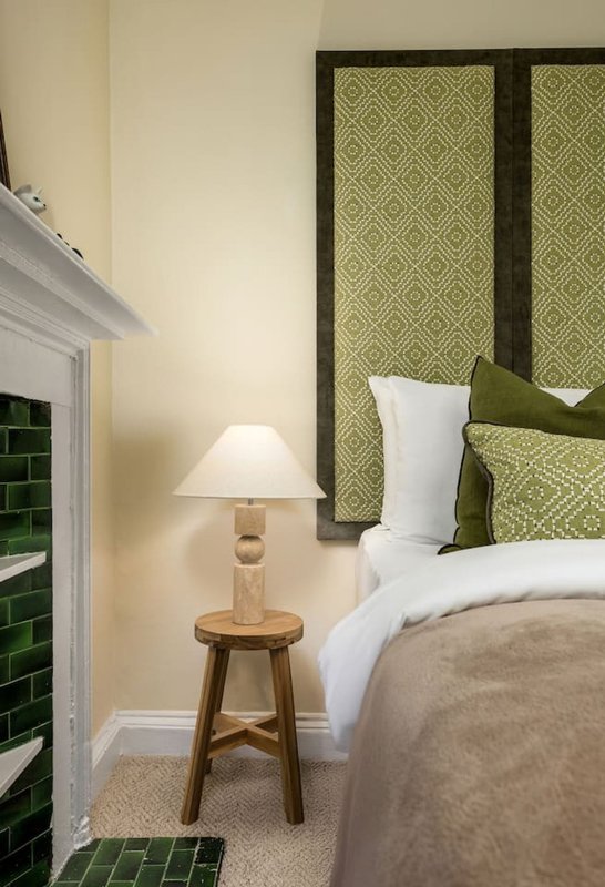 Bedroom with double bed, green headboard, wooden side table with lamp and fireplace