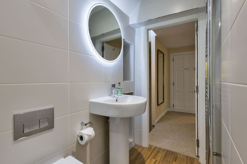 Modern bathroom with illuminated circular mirror, white pedestal sink, and tiled walls
