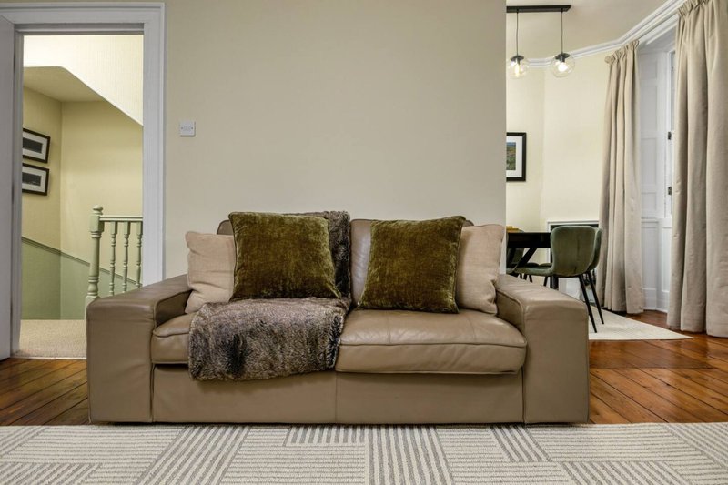 Beige upholstered sofa with green cushions and throw blanket in open-plan living area