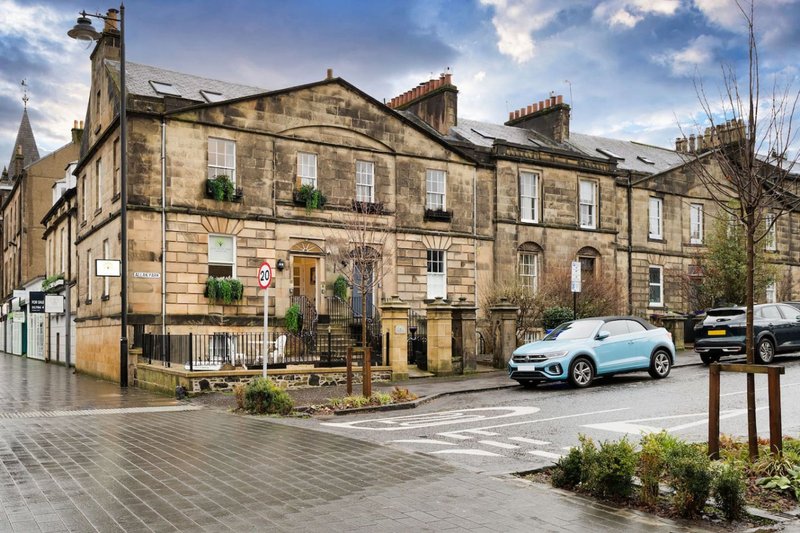 Victorian stone building with parked cars and paved street forecourt