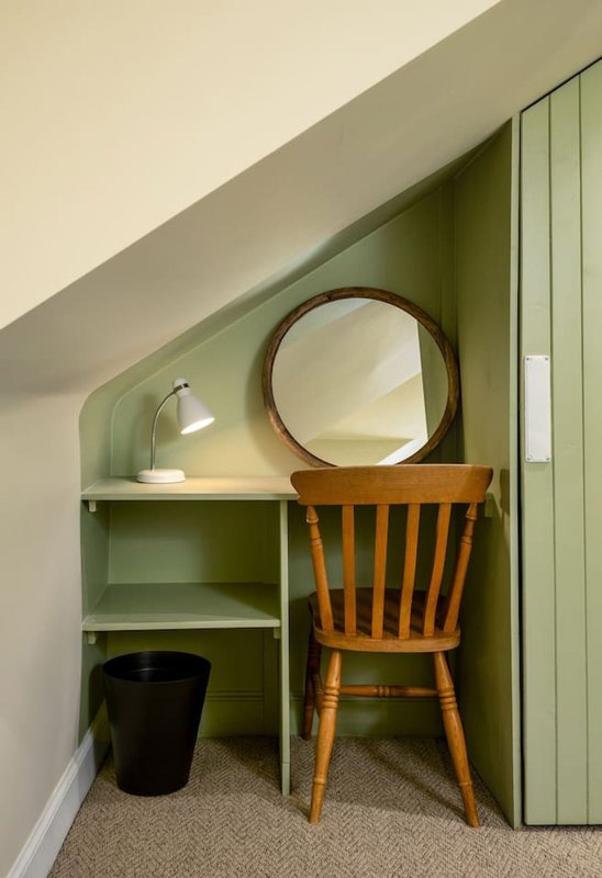 Attic alcove with green built-in shelving, round mirror, wooden chair and desk lamp