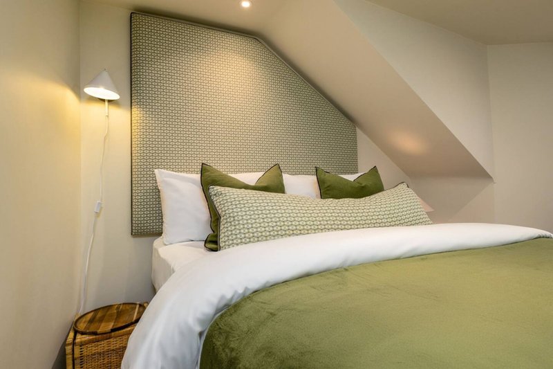 Modern bedroom with olive green bedding, white pillows, angled ceiling and wall lamp
