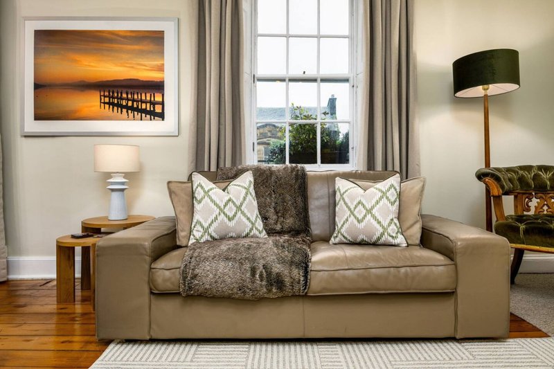 Living room with beige sofa, patterned cushions, throw blanket, framed artwork and window view