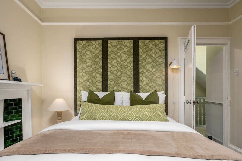 Modern bedroom with green upholstered headboard, white bedding, and decorative pillows