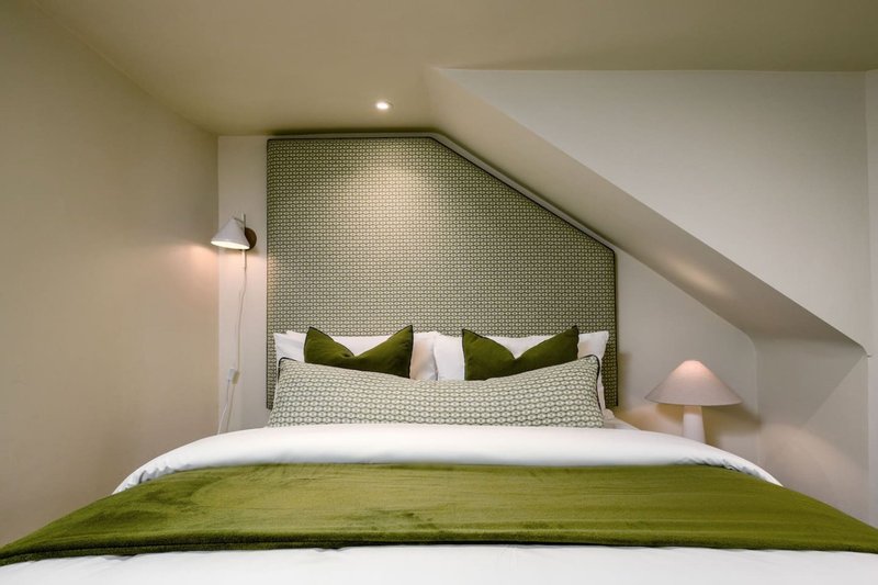 Attic bedroom with sloped ceiling, double bed with green bedding and white pillows, wall sconces
