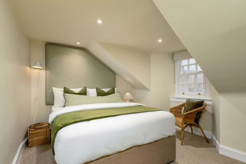 Attic bedroom with double bed, green headboard, wooden chair, and sloped ceiling
