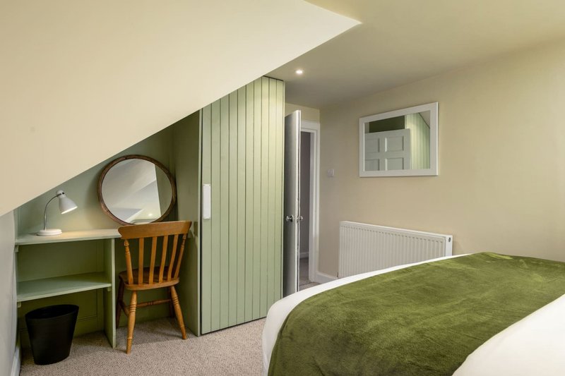 Modern bedroom with green bed, wooden desk, round mirror and sloped ceiling