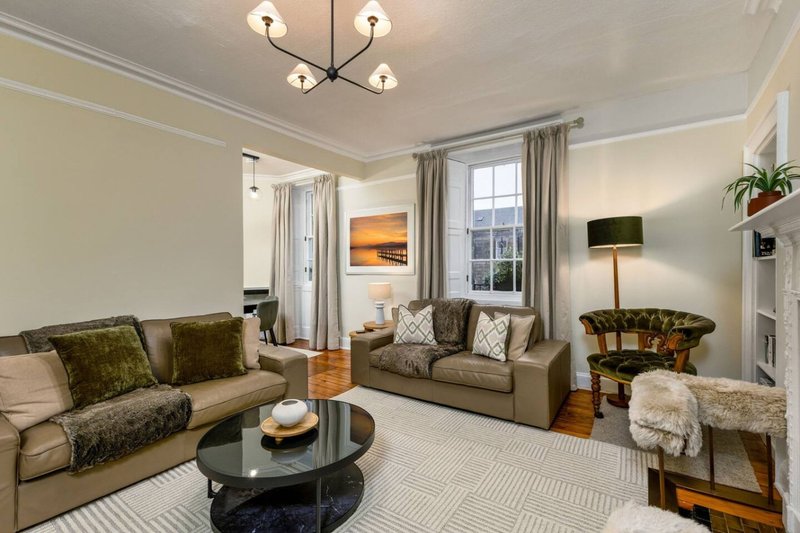 Bright living room with two sofas, round black coffee table, large windows and modern ceiling light