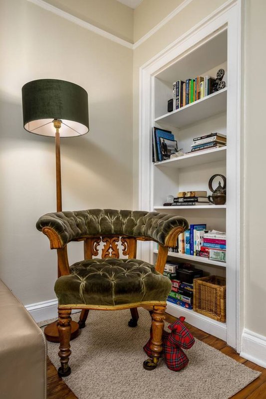 Corner reading nook with green leather armchair, floor lamp, and built-in white shelving with books