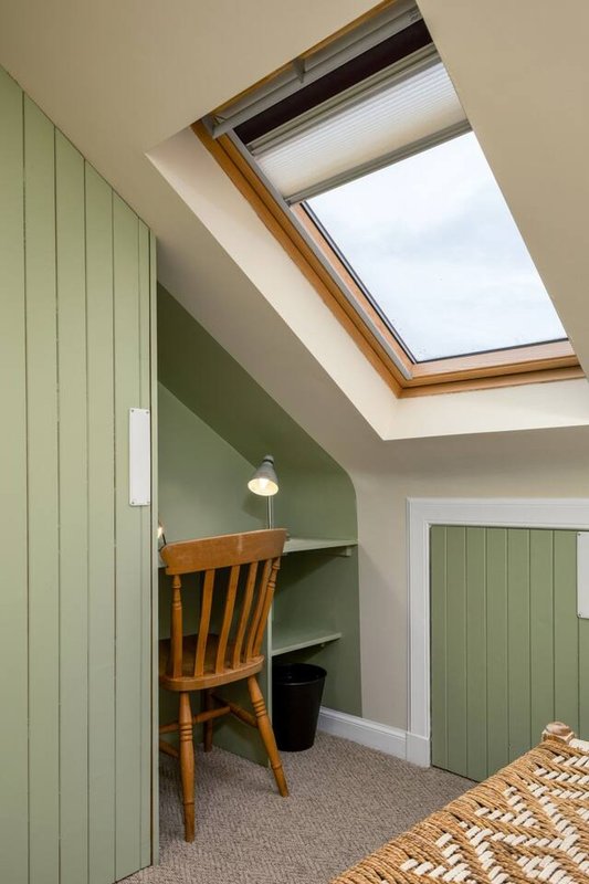 Attic bedroom with skylight, wooden desk, chair, green panelled walls and carpet flooring