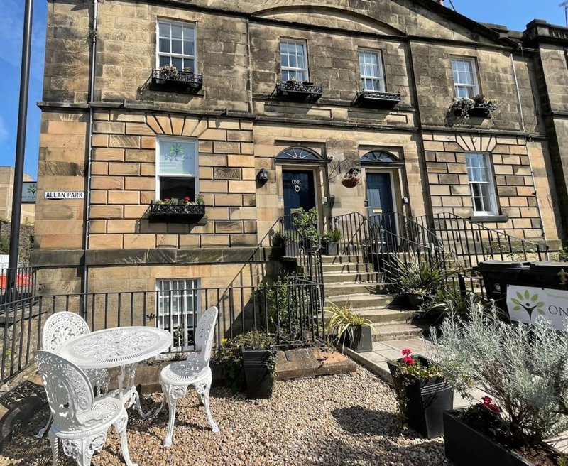 Stone townhouse exterior with front garden, white chairs, potted plants and metal railings