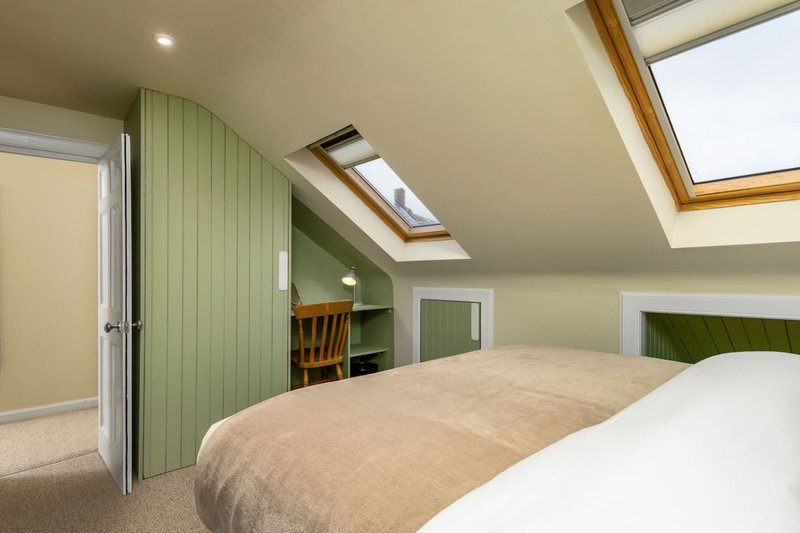 Bright attic bedroom with double bed, green built-in wardrobes and skylight windows