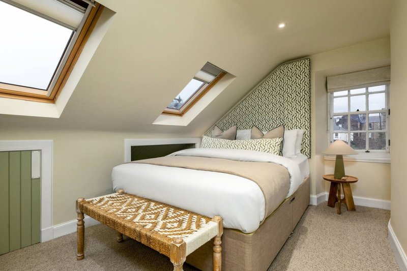 Bright attic bedroom with double bed, patterned headboard, wooden bench, and skylight windows