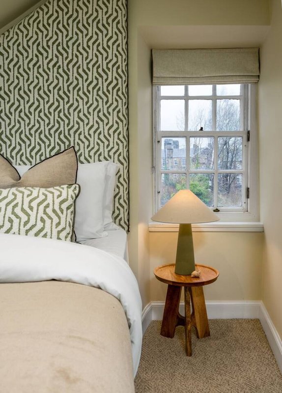 Bedroom corner with patterned headboard, white bedding, wooden side table and window seat