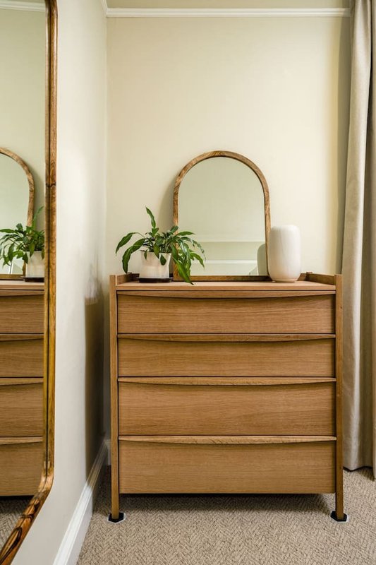 Wooden dresser with arched mirror, potted plant and white vase on top