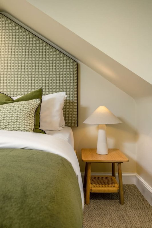 Bedroom with green and white bedding, headboard, wooden nightstand and table lamp