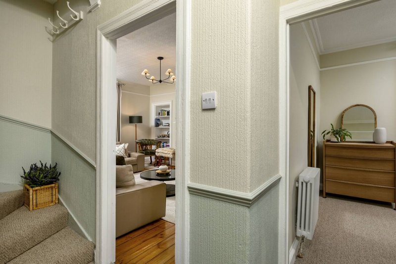 Hallway with stairs, open doorways to living room and bedroom, wooden floor and neutral décor
