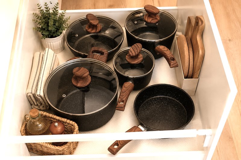 Kitchen drawer organizer displaying non-stick cookware set with wooden handles and potted herbs
