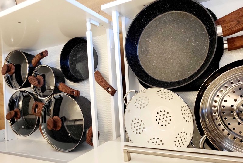 Kitchen cabinet interior with organised cookware including pans, colanders and steamer baskets