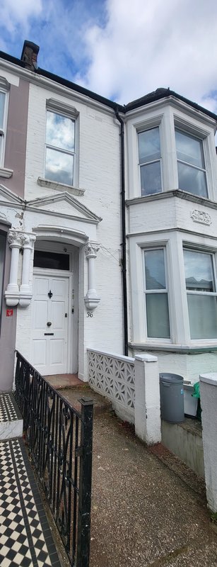 White terraced house exterior with black and white tile path, iron railings and entrance door