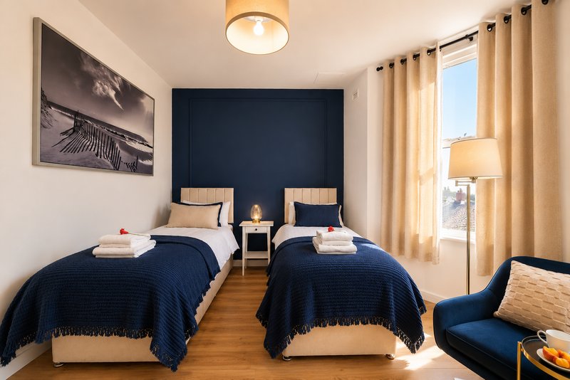 Bright twin bedroom with two single beds, navy feature wall, wooden floor and cream curtains