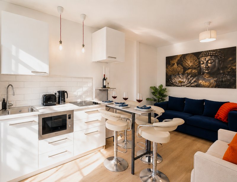 Open-plan kitchen and living area with white cabinetry, bar seating, dark blue sofa and wall art
