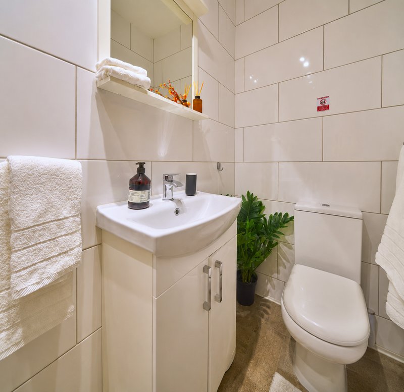 Modern bathroom with white tile walls, vanity sink, mirror, toilet and towel rack