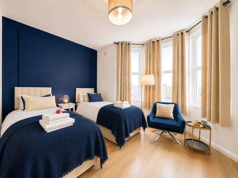 Twin bedroom with navy feature wall, matching bedding, wooden flooring and large windows with curtains