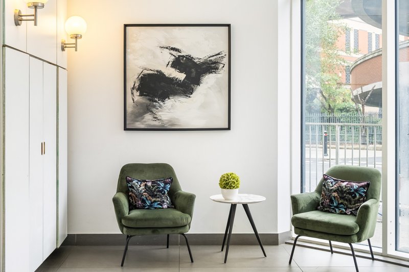 Modern living space with two green armchairs, small round table, framed artwork and large windows