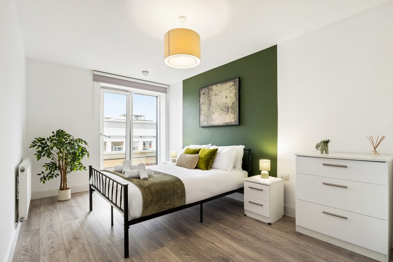 Modern bedroom with double bed, green accent wall, white furniture and natural light from windows