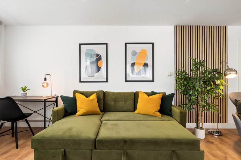 Modern living room with green sofa, yellow cushions, framed artwork and wooden floor