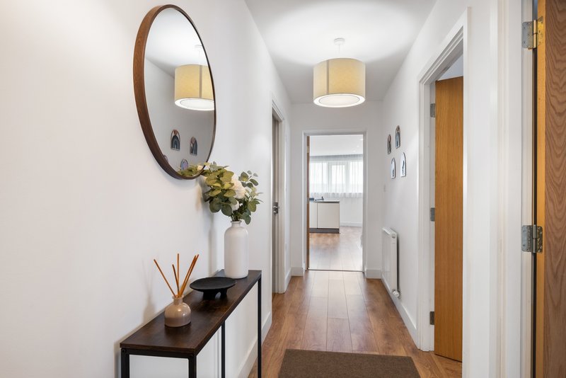Bright hallway with wooden floors, round mirror, console table, pendant light and potted plant