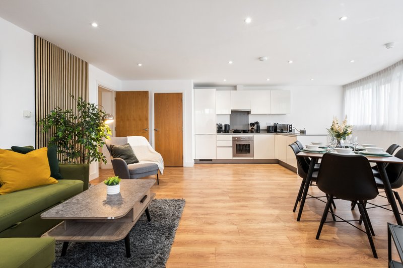 Modern open-plan living space with green sofa, wooden dining table, kitchen, and wooden flooring