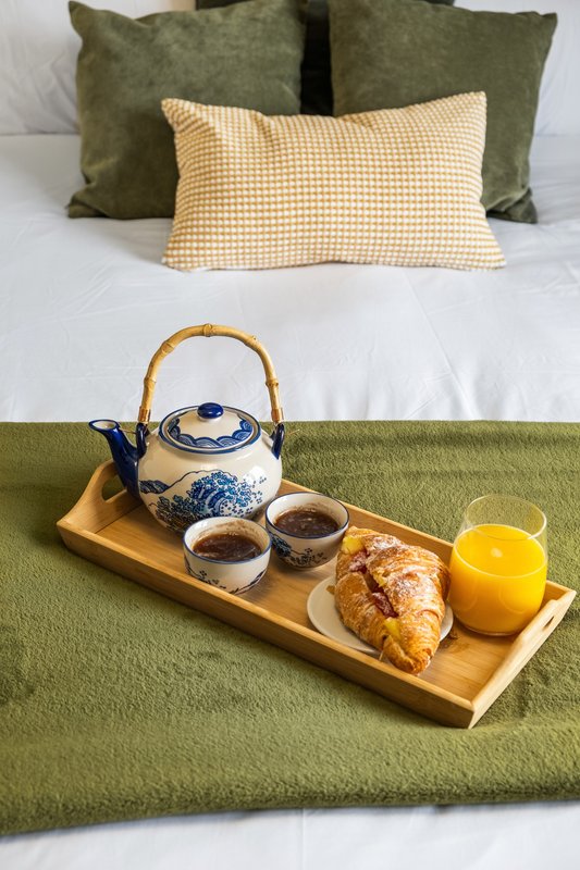 Bed with green and cream pillows, wooden tray with teapot, cups, croissant and juice
