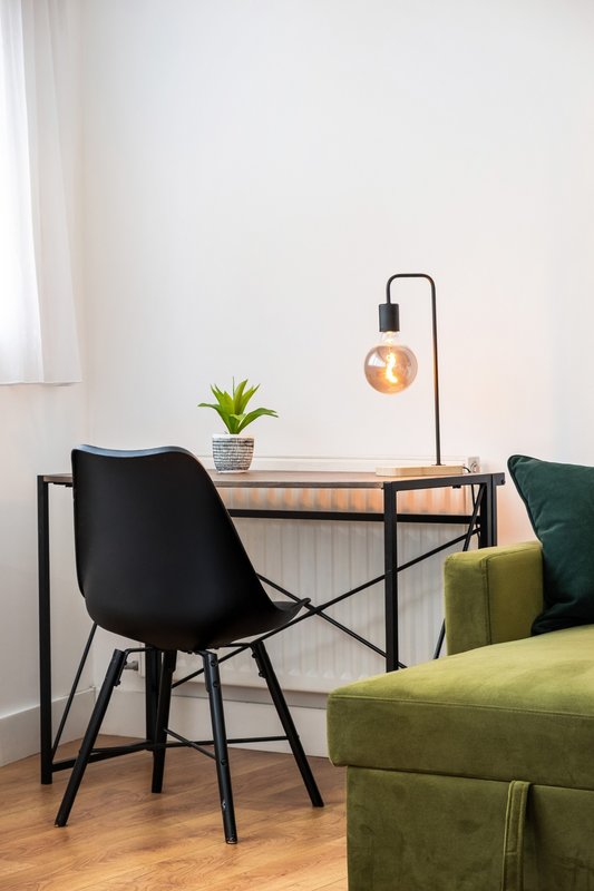 Modern workspace with black chair, desk lamp, small potted plant, and green upholstered sofa