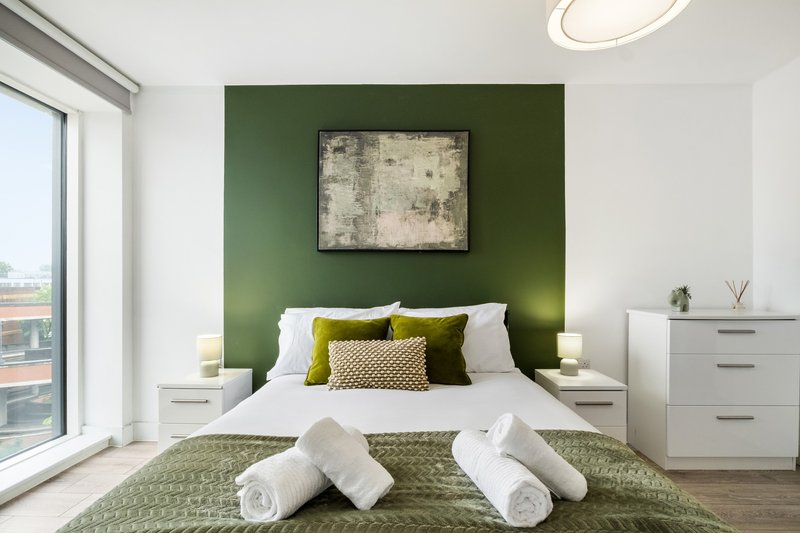 Modern bedroom with green accent wall, double bed, white bedding and rolled towels