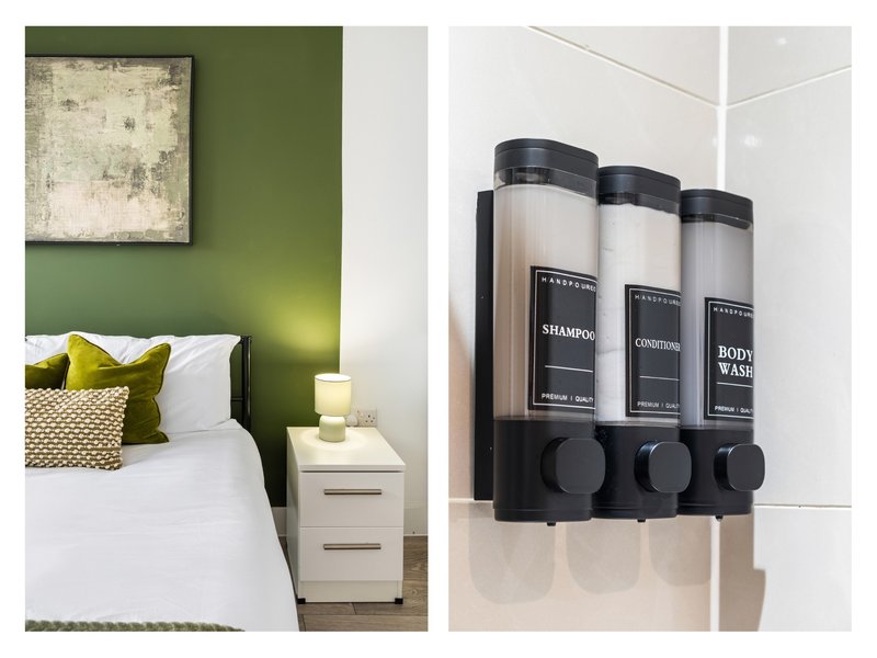 Bedroom with green accent wall, white bedding, yellow pillows, and wall-mounted bathroom toiletry dispensers