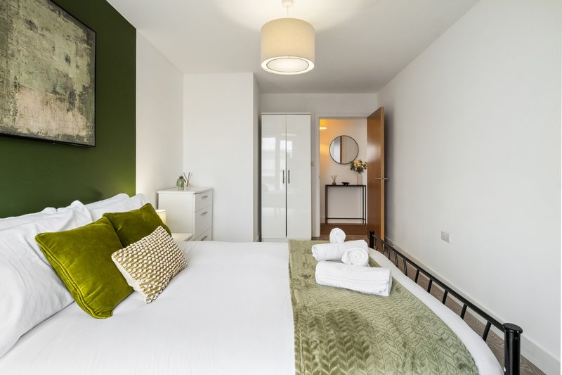 Modern bedroom with double bed, green accent wall, white bedding and coordinating cushions