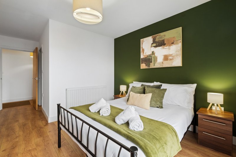 Modern bedroom with double bed, green accent wall, wooden nightstand and ceiling light