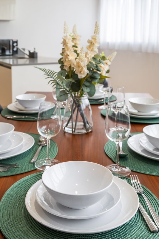 Dining table set for four with white plates, green placemats, and floral centerpiece