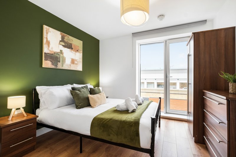 Modern bedroom with green accent wall, double bed, wooden furniture and balcony access